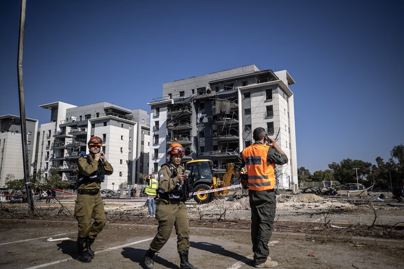 Personnel in uniform stand in front of damaged apartment buildings