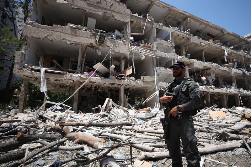 Man in uniform stands in front of building with its facade blown off