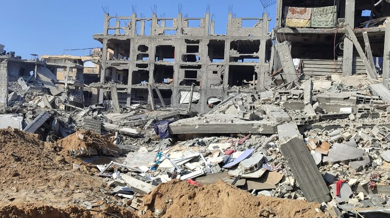 Landscape view of skeleton of three-story building with rubble strewn in front of it
