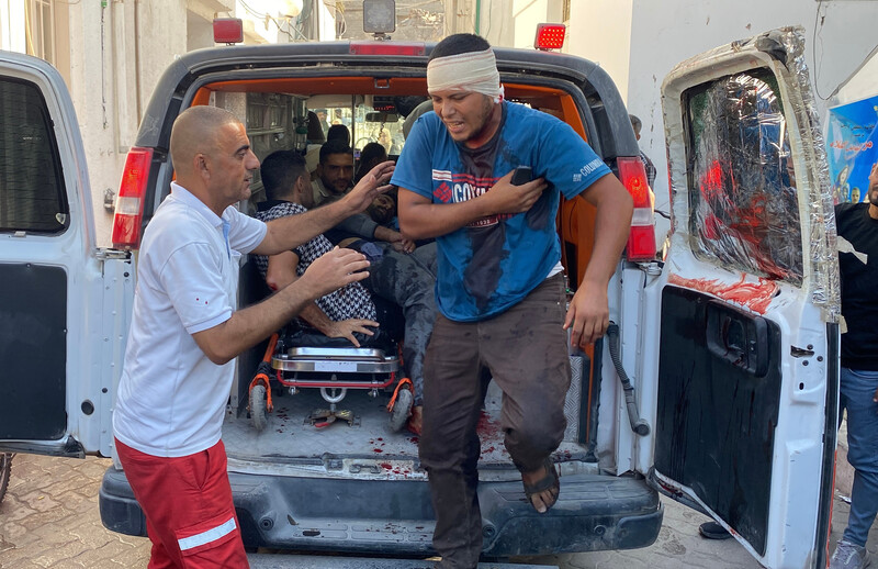 A bandaged man and a paramedic outside the back of an ambulance
