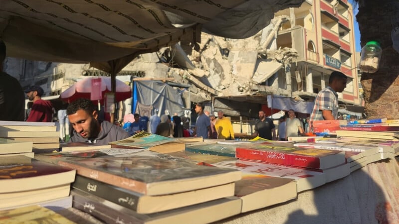 A  pile on the books in the foreground and man apparently reading behind