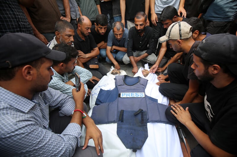 A group of mourners around a coffin with a press vest laid on top