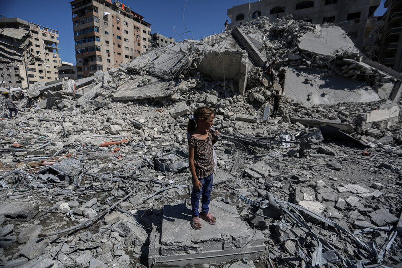 A girl, wearing blue pants and a polka dot top, stands on top of a massive pile of concrete rubble