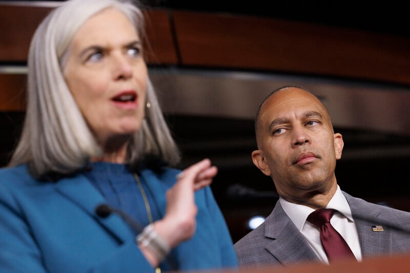 Congresswoman Katherine Clark speaks from a podium as Congressman Hakeem Jeffries looks on