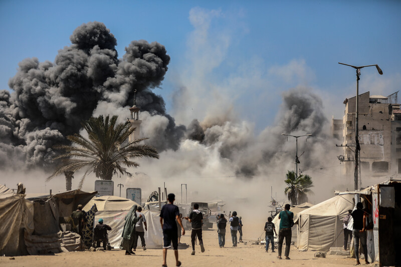 Palestinian bystanders watch smoke billow over Gaza City following an Israeli attack