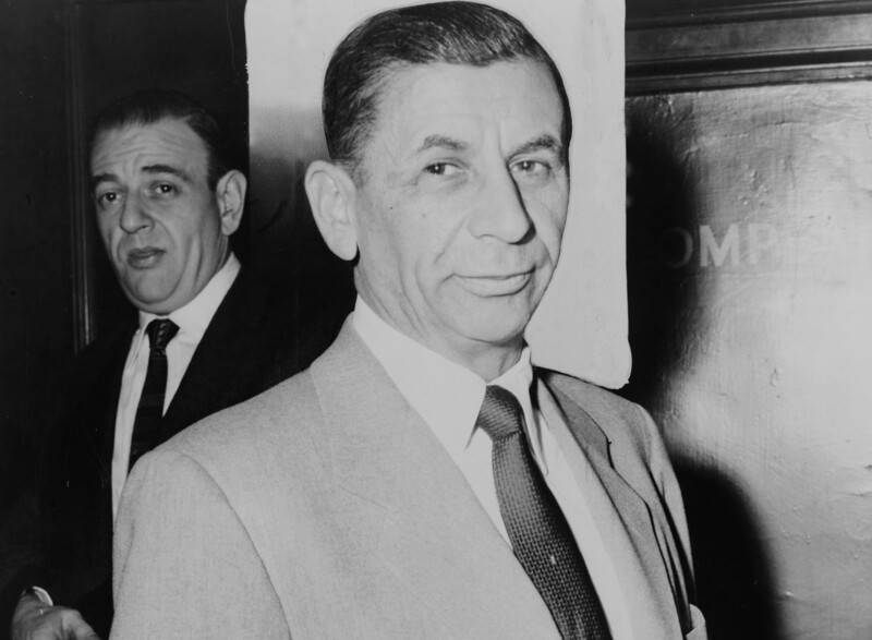 A man in a suit flanked by a bodyguard