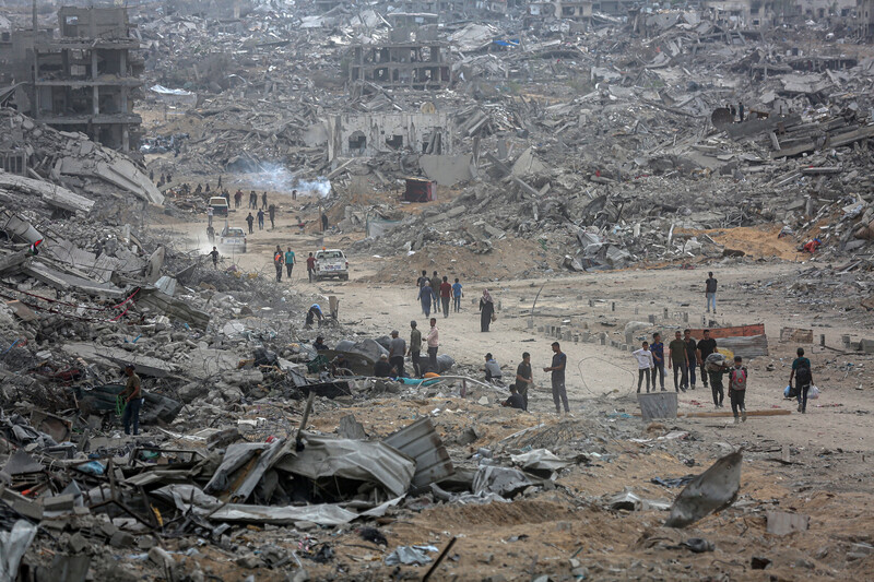 People walk on a road amid a landscape of destruction.