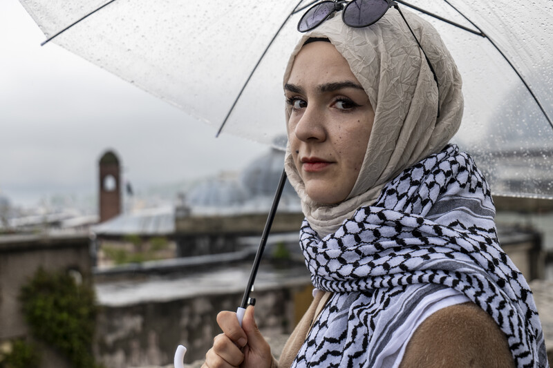 A woman wearing a Palestinian checkered scarf is holding an umbrella