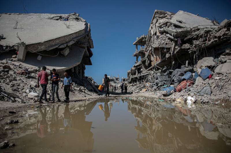 Several Palestinians in Jabaliya walk by standing water and demolished buildings
