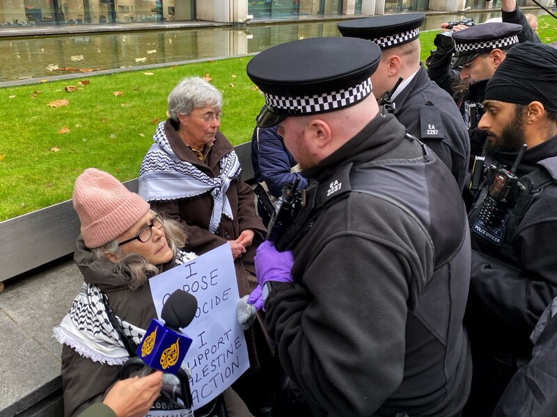 Police about to arrest two women holding signs saying they support Palestine Action