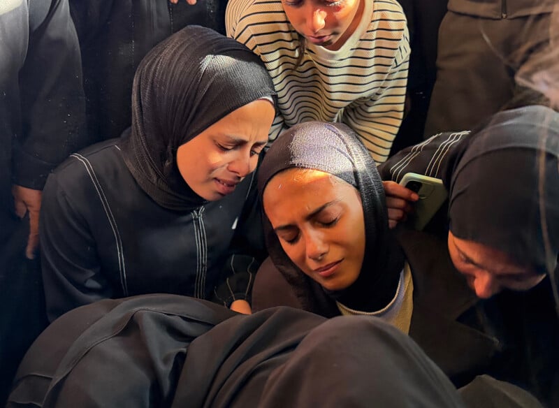 Women wearing black clothing embrace each other at a funeral