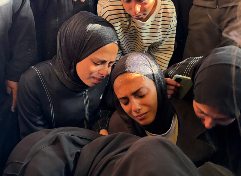 Women wearing black clothing embrace each other at a funeral