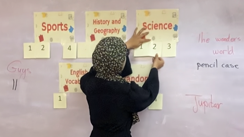 A woman, her back to the camera, attaches several handwritten papers to a board.