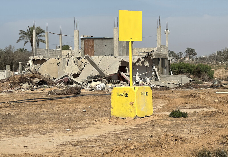 A concrete block painted yellow with a yellow sign stands before the rubble of buildings
