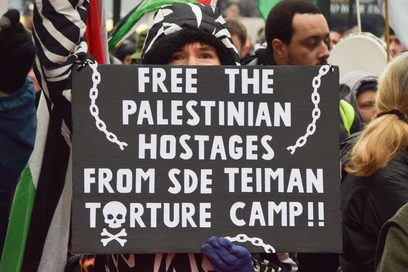 Woman at demonstration holds sign reading "Free the Palestinian hostages from Sde Teiman torture camp"