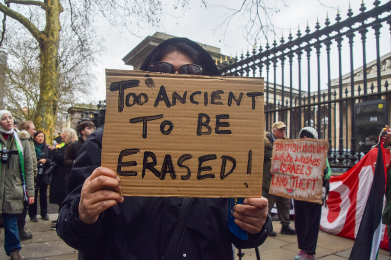 A person holds a sign reading "Too ancient to be erased" with museum and other protesters in background