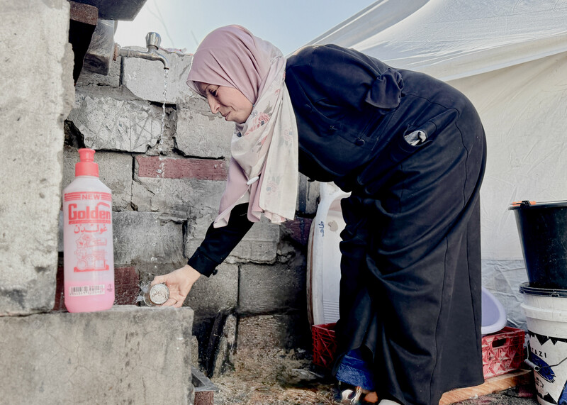 A women is trying to wash a glass cup using only her right hand since her left one is amputated
