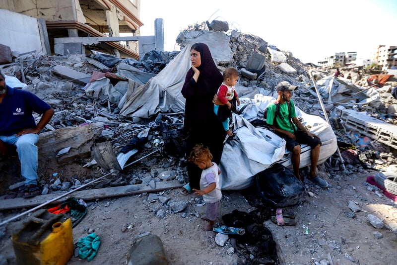 A young woman holds her hand to her face while holding a toddler with a man and young child standing and sitting next to her
