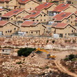 An earth-moving machine works in the foreground with Israeli settlement homes in background