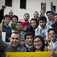 Young man smiles among crowd making victory symbol with their hands