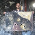 Artist Raed Issa holds up one of his damaged paintings in his bombed-out house in Gaza