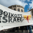 A large banner reading Boikott Israel with an image of a blood-splattered orange slice is held in front of a building