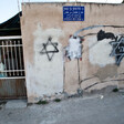 Woman stands behind bars next to walls spray-painted with Stars of David