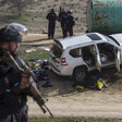 Militarized police officer holding rifle stands in foreground with SUV emptied of its contents in background