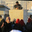 Palestinian woman walk through a checkpoint as an armed Israeli soldier is positioned above them