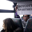 Basil al-Araj sits on bus behind Israeli woman while holding up a sign reading Boycott Apartheid