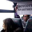 Basil al-Araj sits on bus behind Israeli woman while holding up a sign reading Boycott Apartheid
