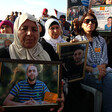 Women sitting on chairs hold photos of men being detained by Israel