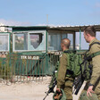Two soldiers carrying heavy weaponry walk in front of checkpoint with shattered windows