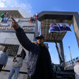A Palestinian Authority officer raises an arm with a pointed index finger as he stands in front of Rafah crossing, decorated with posters of Mahmoud Abbas and Abdulfattah al-Sisi