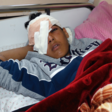 Boy with bandaged head and eye lies on a bed, covered with a blanket