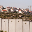 Landscape photo shows a construction crane is above a group of Israeli settlement homes with Israel's concrete wall in the foreground