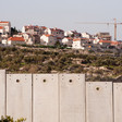 Landscape photo shows a construction crane is above a group of Israeli settlement homes with Israel's concrete wall in the foreground