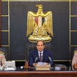 Abdulfattah al-Sisi sits at a desk underneath golden eagle medallion with a military officer on either side of him