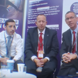 Three men with conference lanyards sit next to each other in a similar pose.