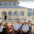 Three Israeli police are seen standing with group of civilians in front of stairs leading up to the Dome of the Rock