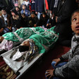 The shrouded bodies of two boys, wrapped in green flags, lay on stretchers while surrounded by mourners