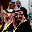 Saudi crown prince is seen smiling from chest up while wearing robe and checkered headdress