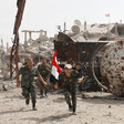 Men in military uniform carry Syrian flag amid rubble of bombed-out buildings