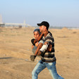 A man carries a boy with a bandaged leg across a sandy landscape