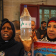 Palestinian women holding up a bottle reading "water and salt." 