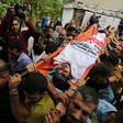 The body of a young man wrapped in a faction flag is carried on a stretcher by a crowd