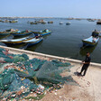 A young man pulls on a pile of fishing nets while standing next to docked boats