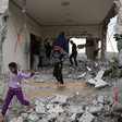A girl and boy walk through the debris of a building with destroyed walls