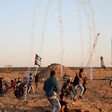 Palestinians protest in front of Gaza boundary fence with trails of tear gas smoke in the sky