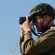 A man in military uniform looks through binoculars